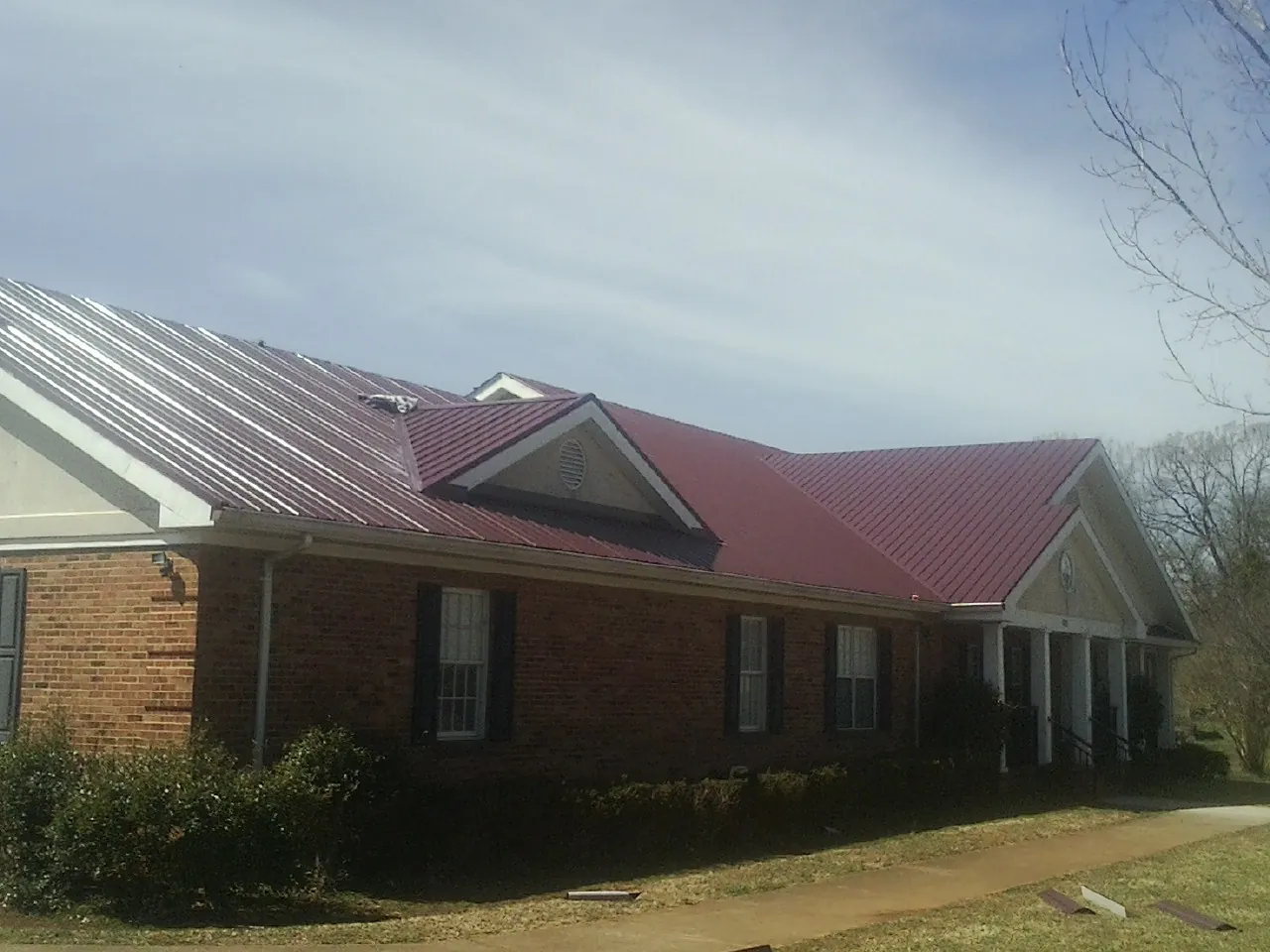 Red metal roof with gabled entries on a long brick building, from a Hail Damage Roof Repair job in Mayview