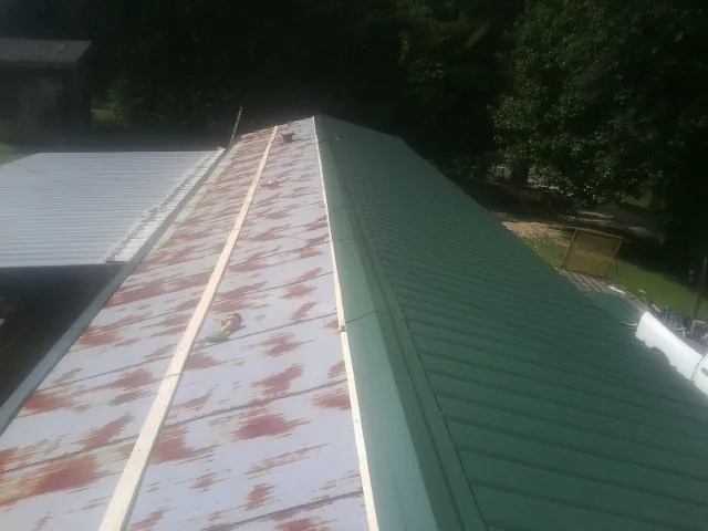 Old rusted panels beside newly installed green metal roofing — Wind Damage Roof Repair by Roofing Brothers in Mayview