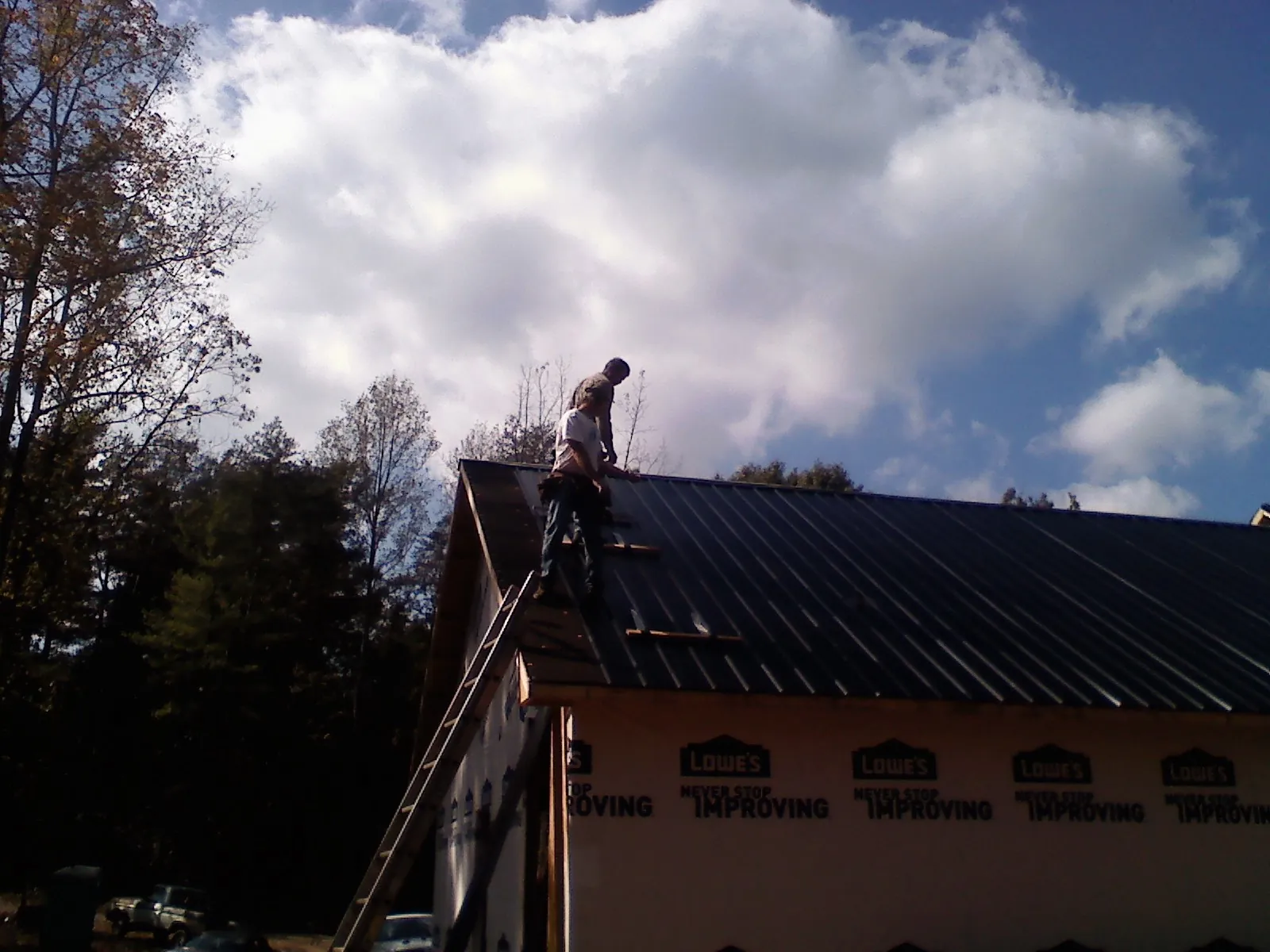 Roofer fastening dark metal panels high against a cloudy sky, from a Roof Inspection job in Mayview