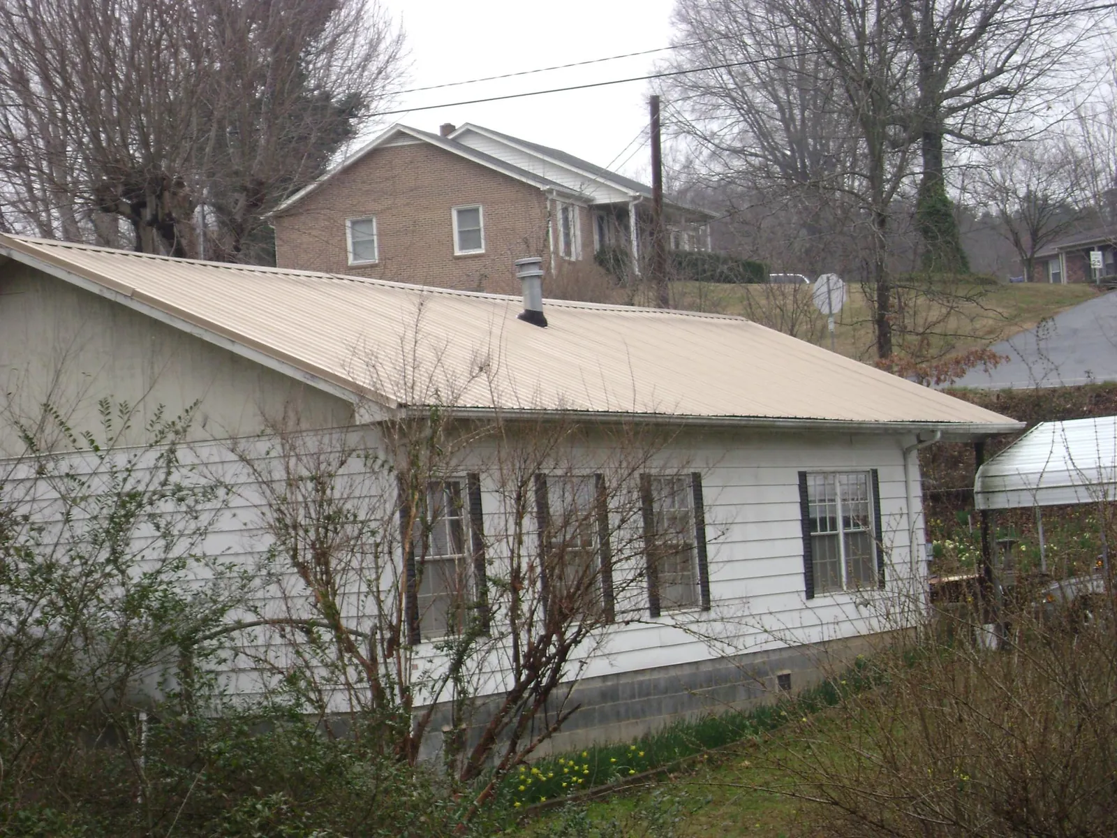 Tan metal roof on a white sided house set into a hillside — Commercial Roofing by Roofing Brothers in Mayview