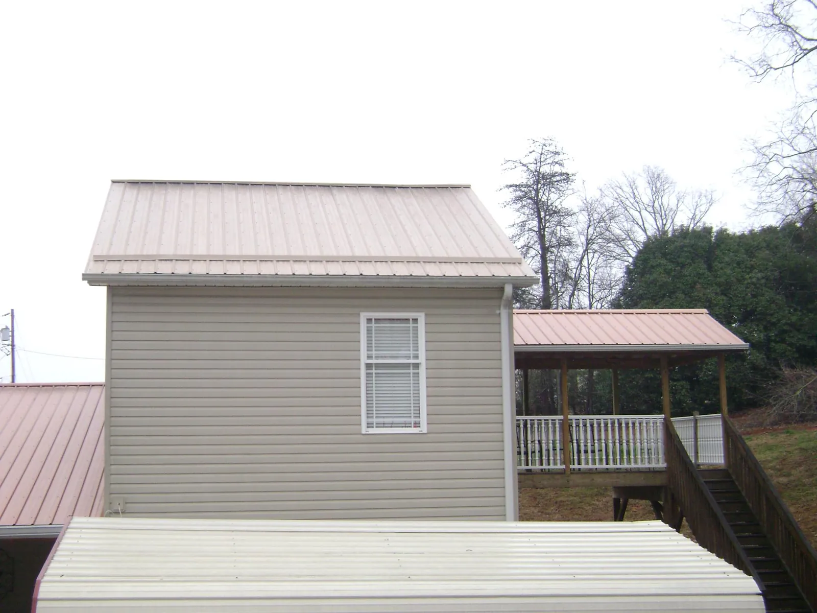 Tan metal roofs on a two story addition and attached porch, from a Roof Replacement job in Mayview